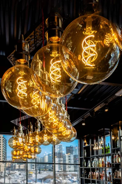 Warm light from beautiful lamps on the ceiling of the bar, against the backdrop of cold lighting from the window on a winter day with a view of the city. drink alcohol and keep warm in the restaurant.