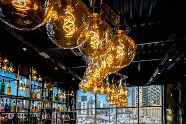 Warm light from beautiful lamps on the ceiling of the bar, against the backdrop of cold lighting from the window on a winter day with a view of the city. drink alcohol and keep warm in the restaurant.