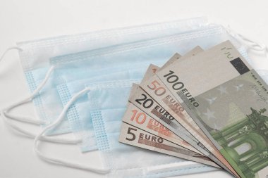 Tıbbi maskeler ve avro banknotları beyaz arka planda izole edilmiş, küresel salgın COVID-19 salgınına karşı ilaç ve ilaç verme kavramı ve Coronavirus ile mücadele.