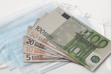Tıbbi maskeler ve avro banknotları beyaz arka planda izole edilmiş, küresel salgın COVID-19 salgınına karşı ilaç ve ilaç verme kavramı ve Coronavirus ile mücadele.