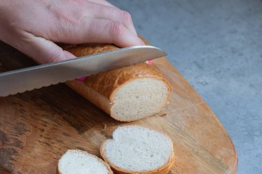 Gri bir tezgahın üzerinde duran uzun ve özel bir tahta üzerinde taze ekmek dilimleme işlemi. Özel ekmek bıçağıyla taze ekmek kes..
