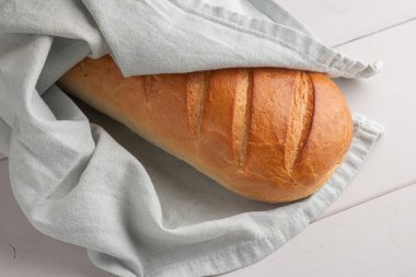 Taze hamur işleri, taze beyaz ekmek bir havlunun içindeki ahşap masada yatıyor.