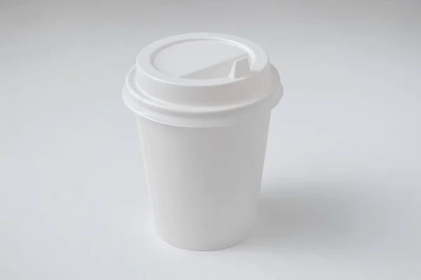 Side view of a white disposable cup for cappuccino and espresso coffee with a white cap on a white background.