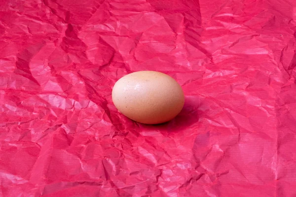 Ein Braunes Hühnerei Liegt Auf Einem Karminroten Zerknüllten Papierhintergrund — Stockfoto