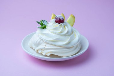 Beyaz tabakta Pavlova kremalı tatlı ve pembe arka plan. Kremalı, yuvarlak kremalı kremalı krema, nane yapraklı ve kirazlı tatlı.