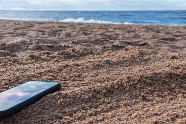 Gri kumlara gömülü cep telefonu, tatildeyken kumsalda akıllı telefonunu kaybetmek..
