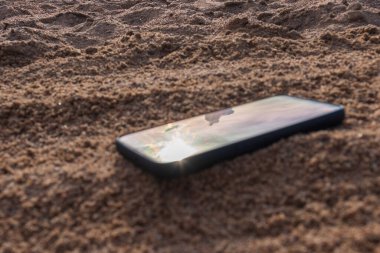 Gri kumlara gömülü cep telefonu, tatildeyken kumsalda akıllı telefonunu kaybetmek..