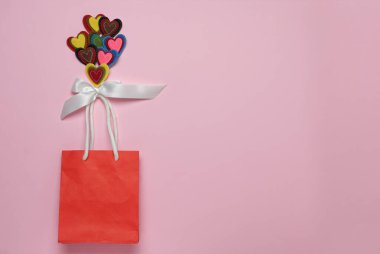 Renkli parlak kalpler, beyaz kurdeleli balonlar, pembe pastel arka planda, kırmızı bir hediye çantası, sevgililer günü tatili konsepti, düz yatış.