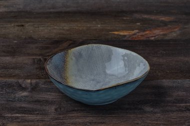 Yuvarlak, yüksek, koyu kahverengi ahşap arka planda pastel renkli boş bir tabak. Yan görünüm.