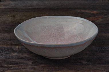 Yuvarlak, yüksek, koyu kahverengi ahşap arka planda pastel renkli boş bir tabak. Yan görünüm.