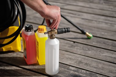 Bir adam, temizlik maddesini yüksek basınçlı mini yıkama makinesine dökmek için köpük jeneratörünün kapağını açar.