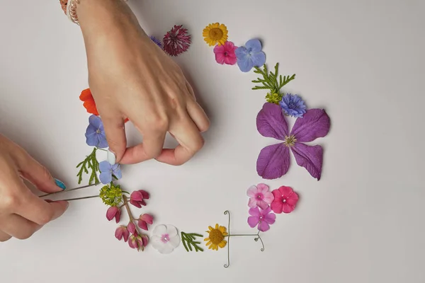 the girl makes a frame of flowers with her hands. Beautiful round frame from a colored flower. Circle made from fresh flowers and leaves on a light gray background.