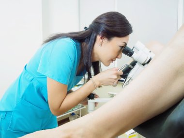 Asian gynecologist examining patient in hospital using a colposcope clipart