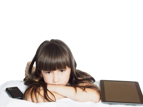 Грустный кавказский ребенок девочка сестра лежит на кровати с мобильным телефоном и планшетным ПК изолированы — стоковое фото
