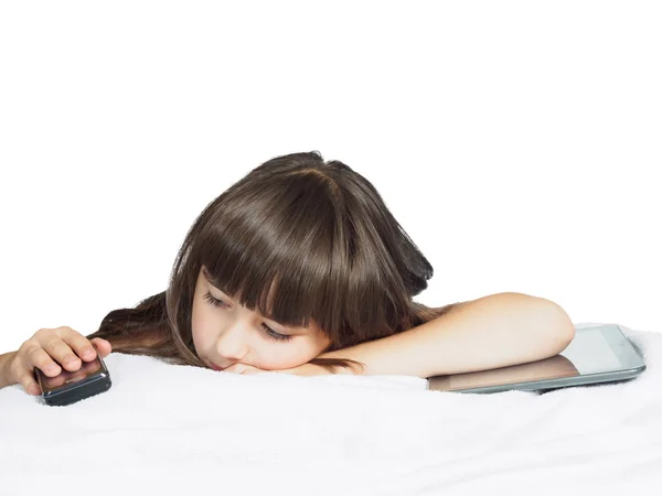 Triste caucasien enfant enfant fille soeur couché sur le lit avec téléphone mobile et tablette pc isolé — Photo