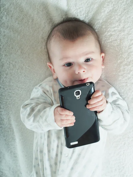 Kleiner Junge hält Smartphone im Bett Stockbild