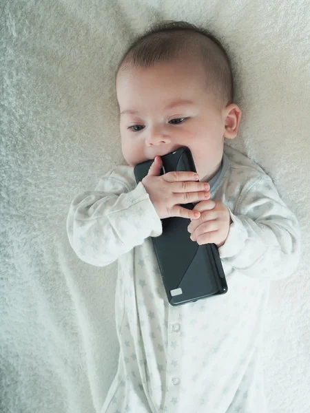 Kleiner Junge hält Smartphone im Bett lizenzfreie Stockbilder