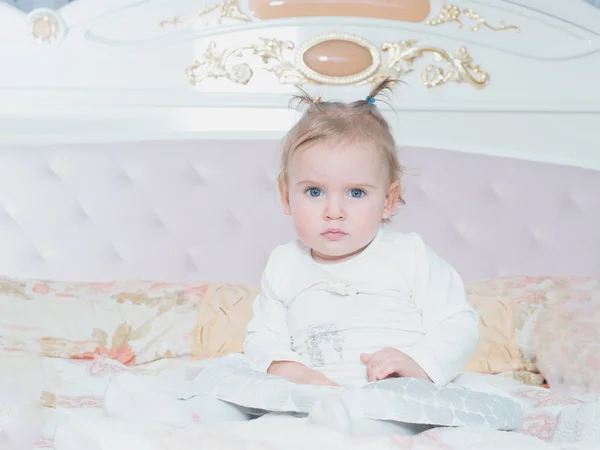 Small caucasian child girl sitting on the bed at home — Stock Photo, Image