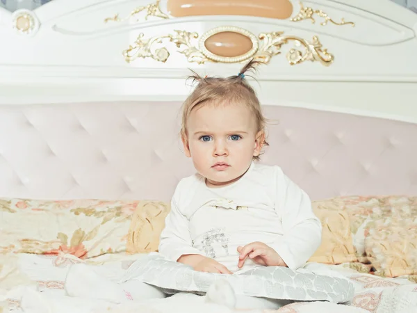 Small caucasian child girl sitting on the bed at home — Stock Photo, Image