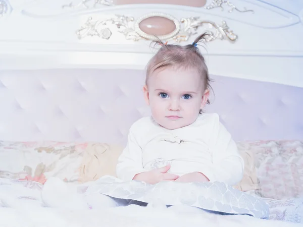 Small caucasian child girl sitting on the bed at home — Stock Photo, Image