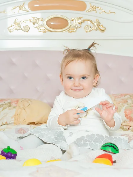 Menina pequena caucasiana brincar com brinquedos na cama em casa — Fotografia de Stock