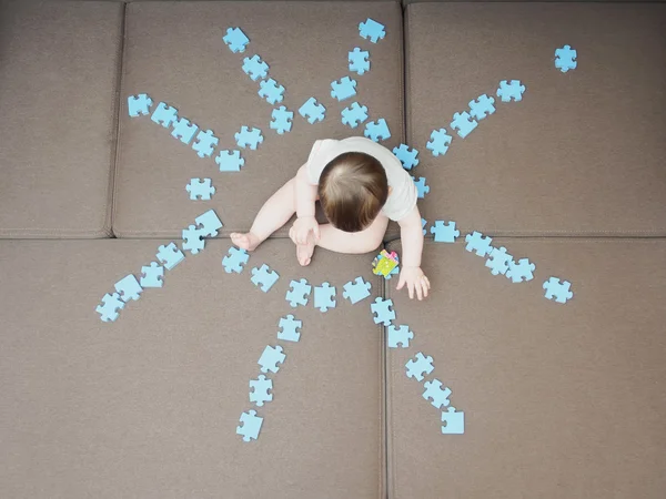 Chłopiec dziecko siedzi w środku puzzli złożyć jako kształt słońca na kanapie w domu pokój dzienny — Zdjęcie stockowe