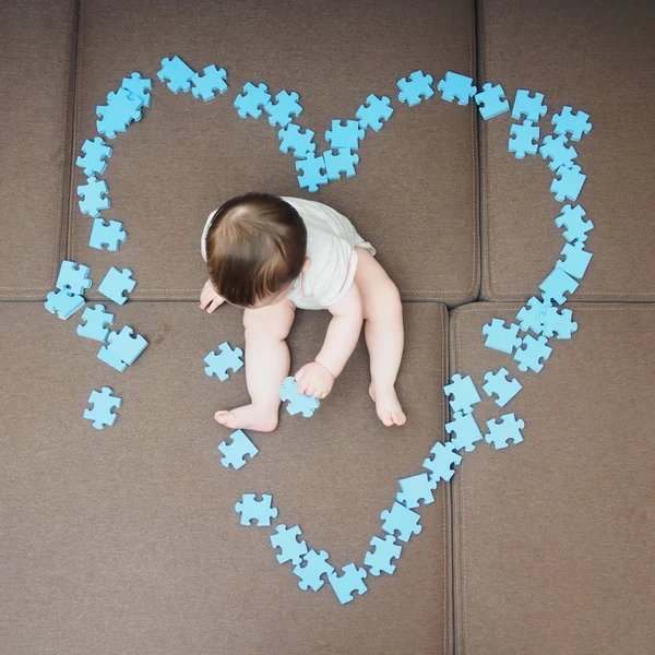 Niño sentado en el medio de piezas del rompecabezas doblado como forma de corazón en el sofá en casa sala de estar —  Fotos de Stock