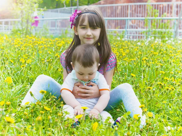 Portrait of brother and sister together sitting in dandelion field — Stock Photo, Image