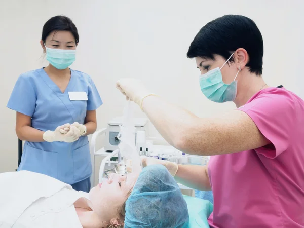 Procedimiento de cosmetología rejuvenecimiento, revitalización, nutrición de la piel. Médico con enfermera haciendo máscara de crema de belleza . — Foto de Stock