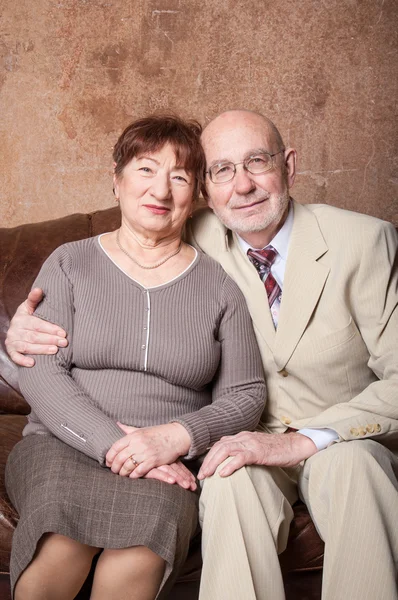 Linda pareja de ancianos sentarse en un sofá marrón —  Fotos de Stock