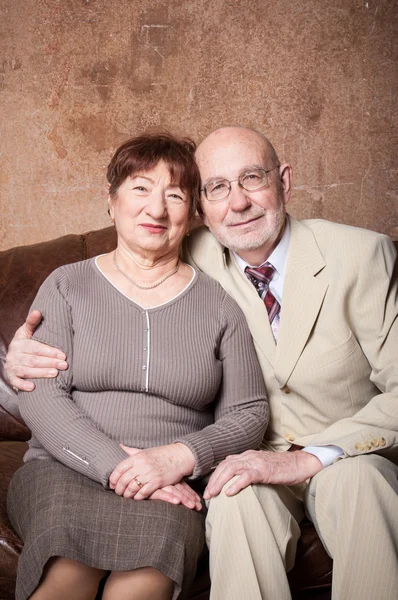 Linda pareja de ancianos sentarse en un sofá marrón —  Fotos de Stock