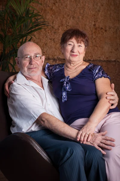 Casal de idosos bonito sentar em um sofá marrom — Fotografia de Stock