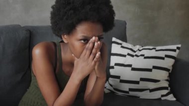 Kanepede oturan düşünceli yüzlü Afro-Amerikalı kadın.