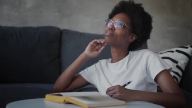 Afro-Amerikalı kız rahat bir odada deftere yazıyor.