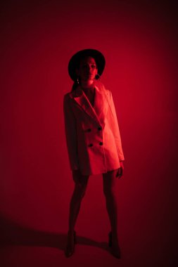 Beyaz takım elbiseli ve siyah şapkalı genç kız. Kıyafet konsepti. Kırmızı ışık. Kırmızı arkaplan