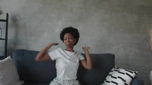 アフリカ系アメリカ人の女の子ダンスとともに彼女の携帯電話でザカウチに居心地の良い部屋 — ストック動画