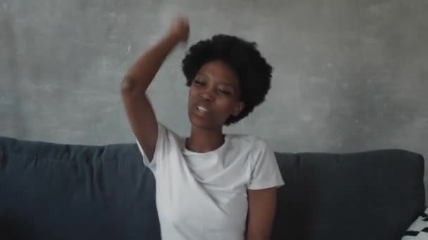 Afro-Amerikaans meisje dansen met haar telefoon op de bank in een gezellige kamer — Stockvideo