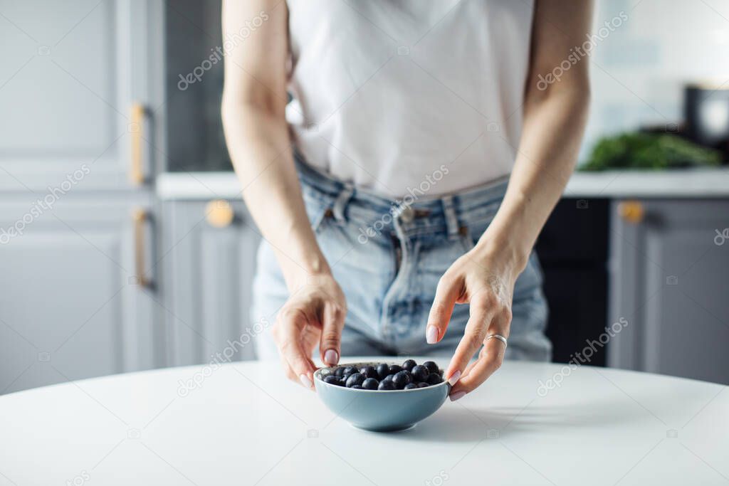 Womans hands take blueberries from the plate. On the background of a beautiful kitchen.