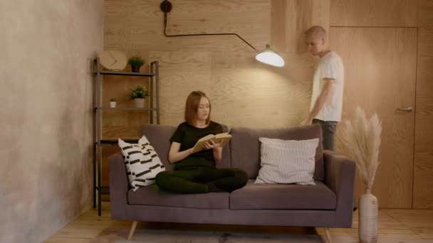 Young couple relax in their cozy apartment. Girl reading a book — Stock Video