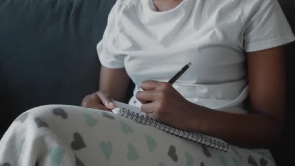 African American girl writes in a notebook in a cozy room — Stock Video