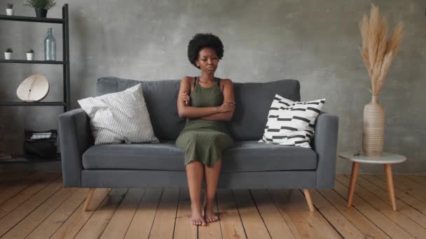 Olycklig afroamerikansk kvinna sitter på soffan, flickan är mycket upprörd sitter på soffan i sin lägenhet. — Stockvideo