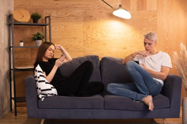 Kanepede oturan genç bir çift. Bir erkekle bir kız telefonlarına bakıyorlar.