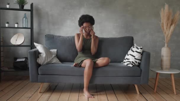 Mulher afro-americana infeliz falando ao telefone, menina irritada falando ao telefone, dispositivo móvel descarregado ou quebrado, problema com o telefone, sentado no sofá — Vídeo de Stock