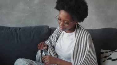 Mutlu Afro-Amerikan genç bayan rahat rahat koltuğa oturup yeni daireye taşındığı için mutlu. Gülümseyen siyah kız oturma odasındaki rahat koltukta dinleniyor.