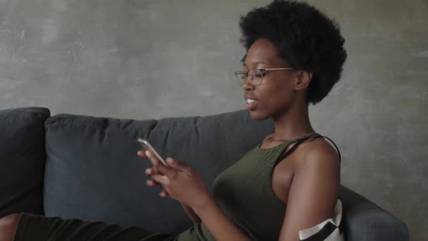 Šťastný africký americký mladá žena sedět relaxovat na útulný gauč rád se přestěhovat do nového bytu. Usmívající se černošky dívka odpočívat na pohodlné pohovce v obývacím pokoji snění — Stock video
