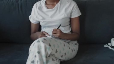 Afro-Amerikalı kız rahat bir odada deftere yazıyor.