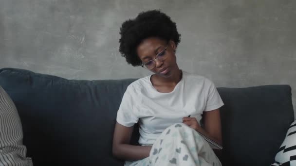 Ragazza afroamericana scrive in un quaderno in una stanza accogliente — Video Stock