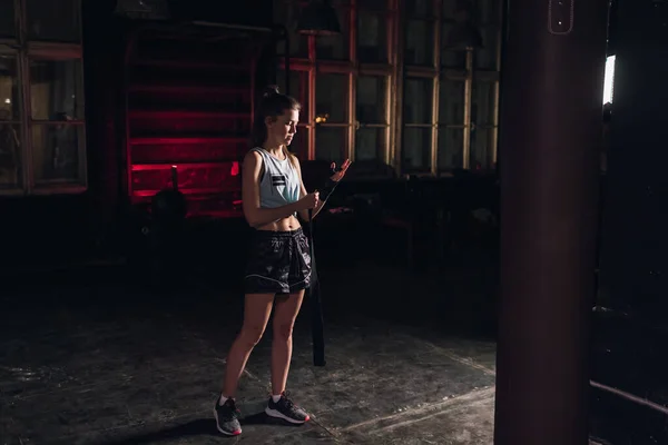 Cool female fighter in boxing bandages trains in gym. Mixed martial arts