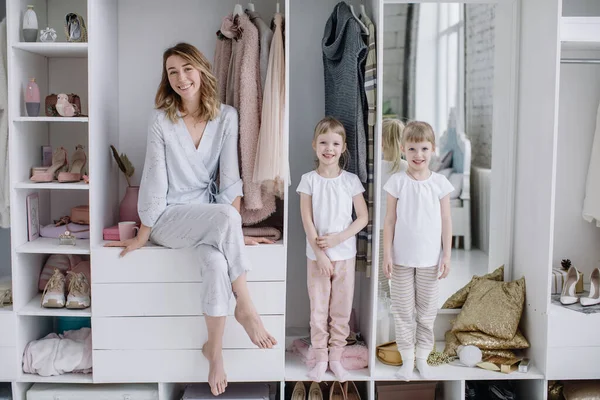 Young mother and her twin daughters are in their modern dressing room looking at the camera Royalty Free Stock Photos