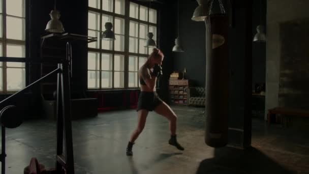 4k vídeo de atlético lutador feminino exercitando com saco de perfuração no ginásio durante o kickboxing e auto-defesa treino — Vídeo de Stock